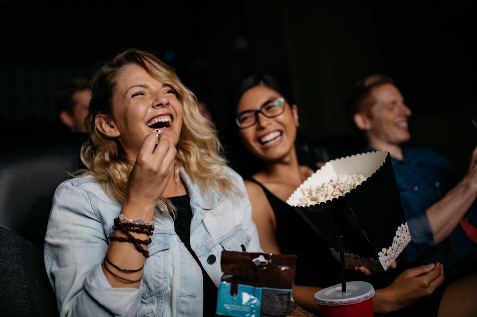 Friends laughing and sharing popcorn in a movie theater